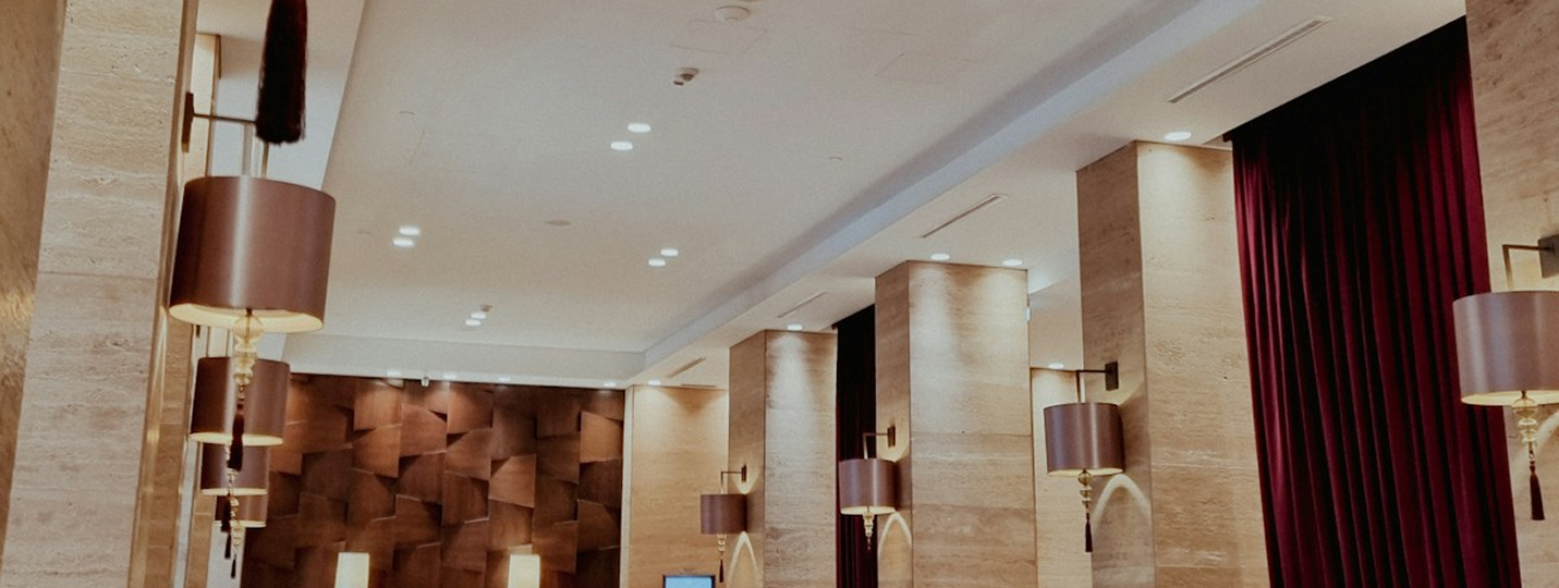 Warmly lit exhibition interior with stone columns, wall lamps and burgundy curtains